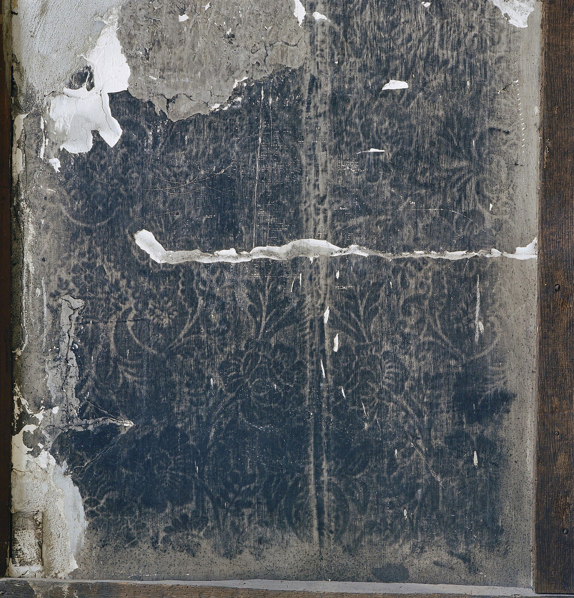 A plaster wall darkened by soot, carrying the damask pattern of the wallpaper that used to cover it, with fragments of paint still clinging at the edges.