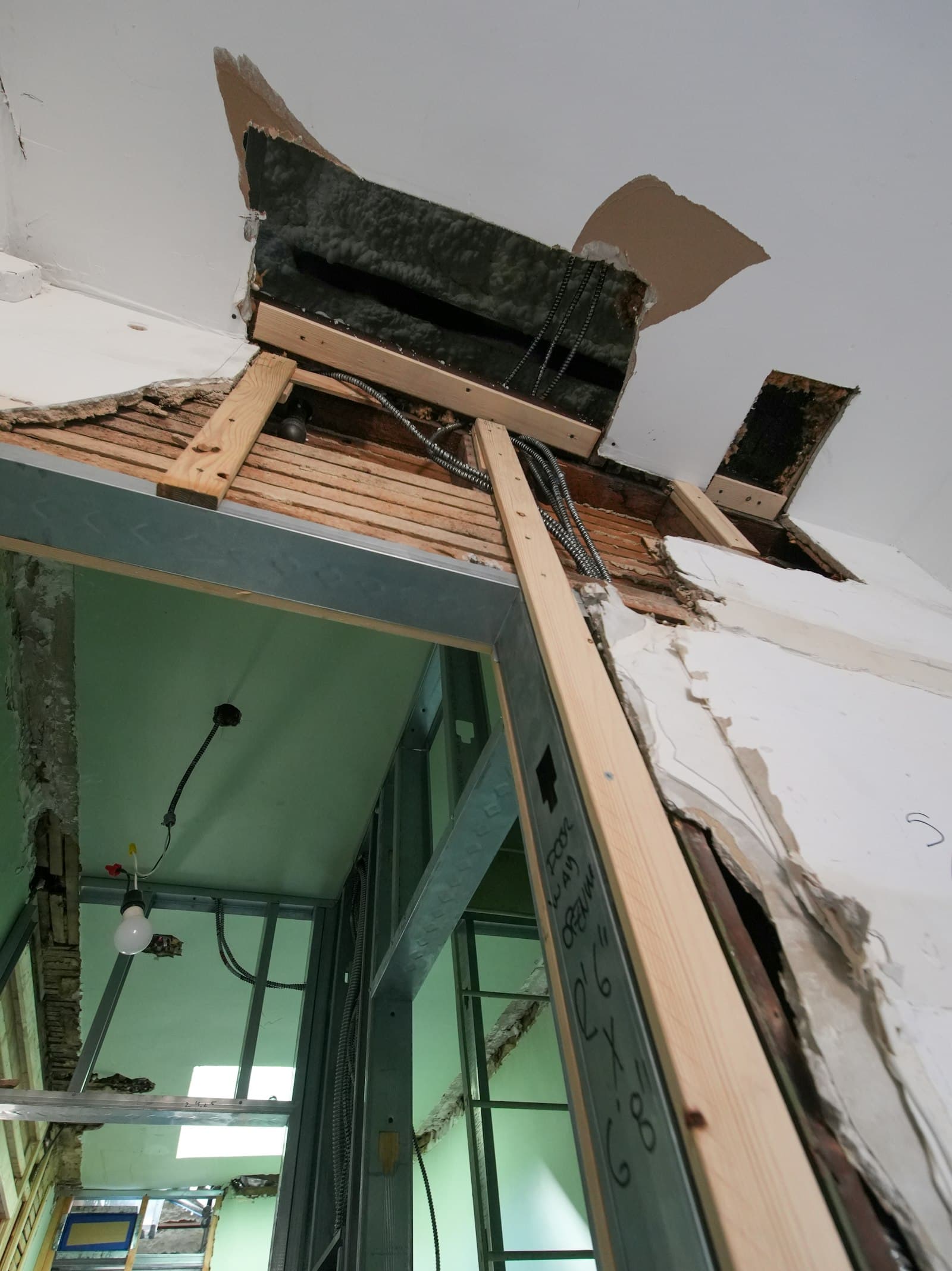 A damaged ceiling and wall opened up, showing wood framing and electrical wiring behind the finish.