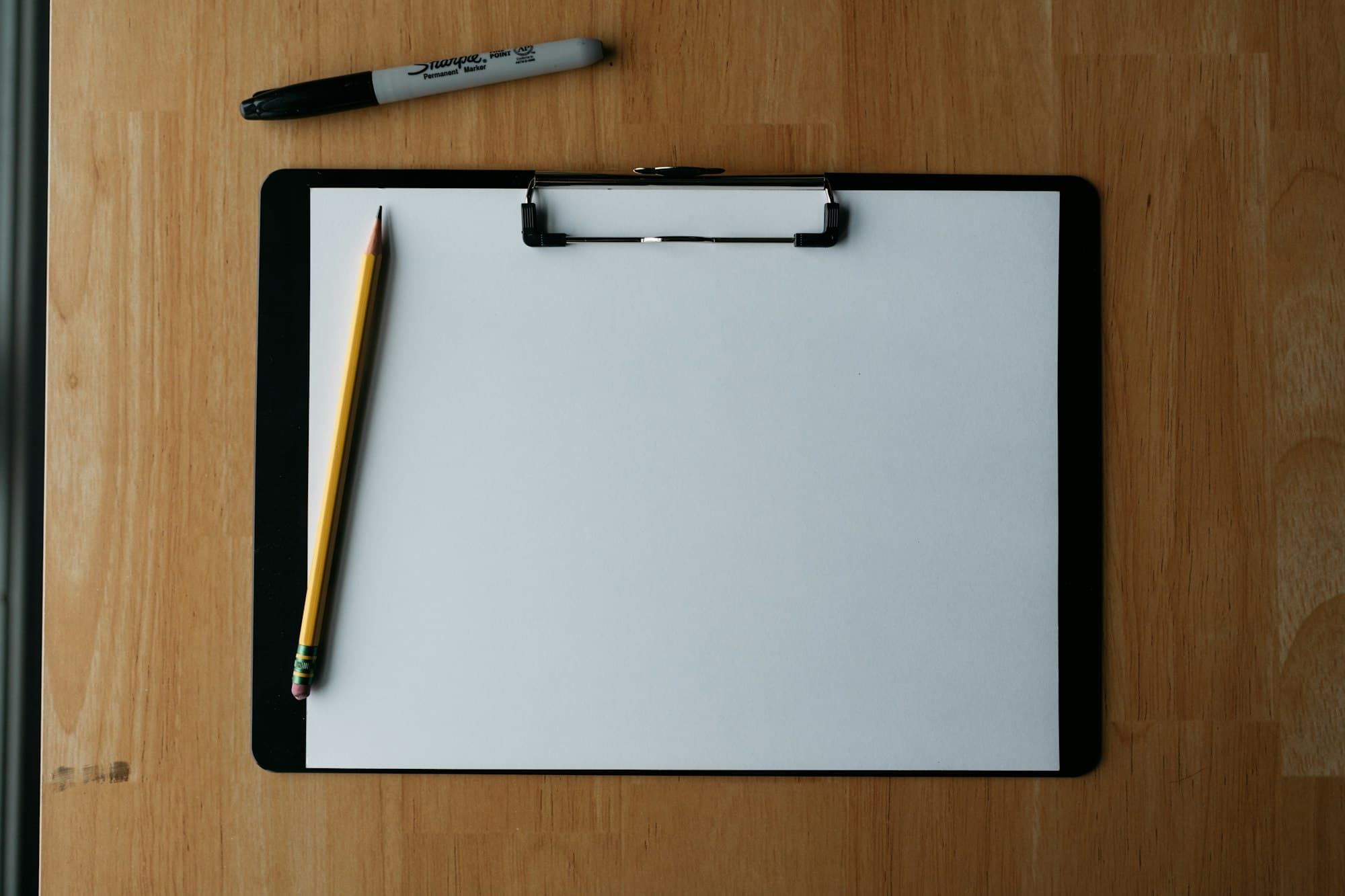 A clipboard with a pencil and pen resting on a wooden surface.
