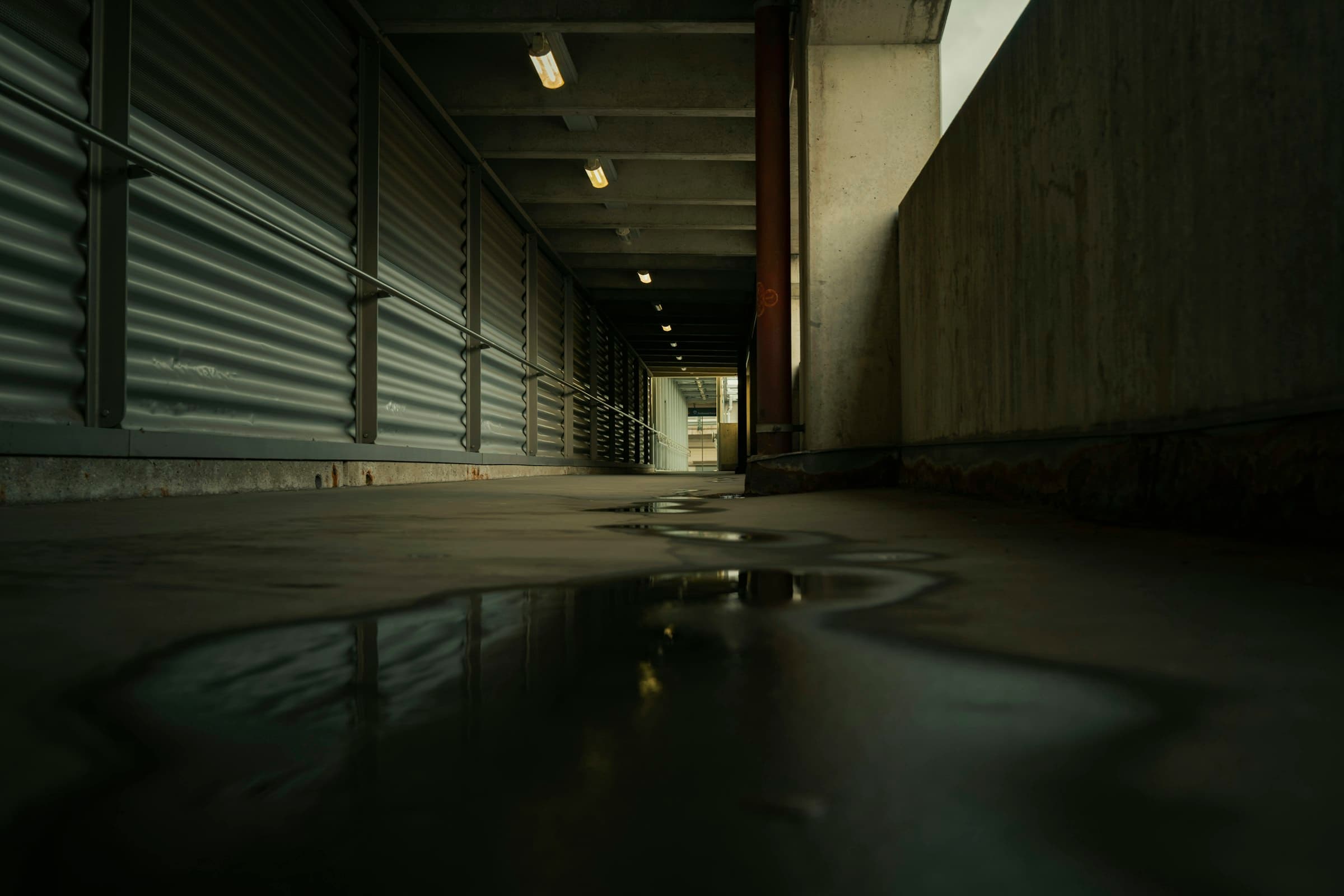 A dark service corridor at night with standing water across the concrete floor, reflecting overhead lights.
