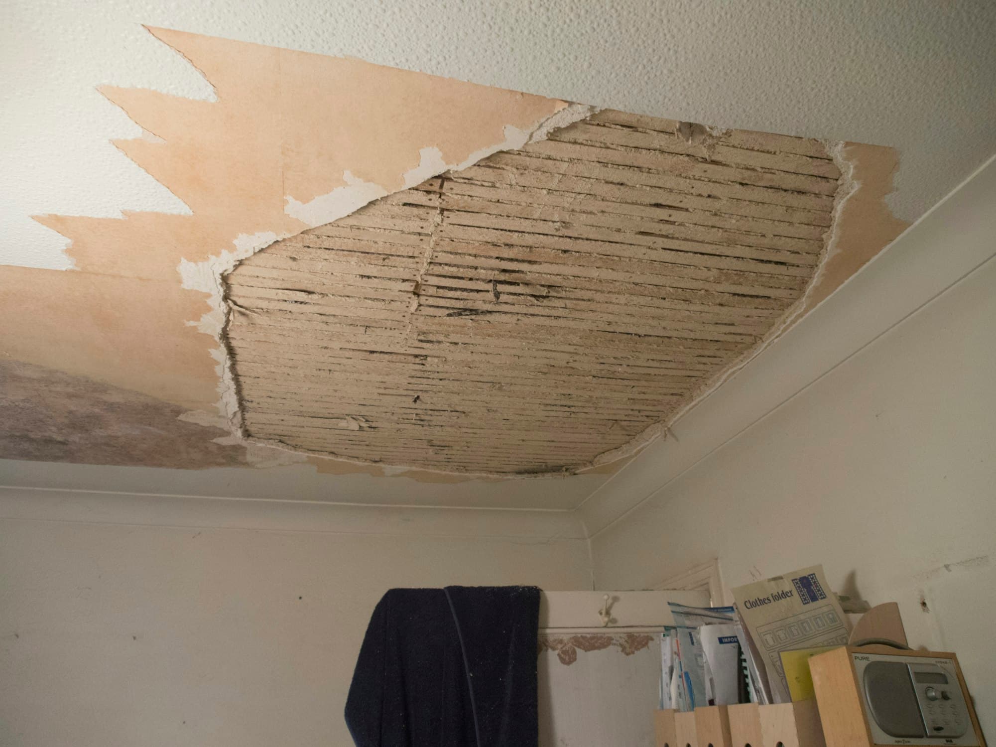 A room with the ceiling torn out, exposing joists and the underside of the floor above.